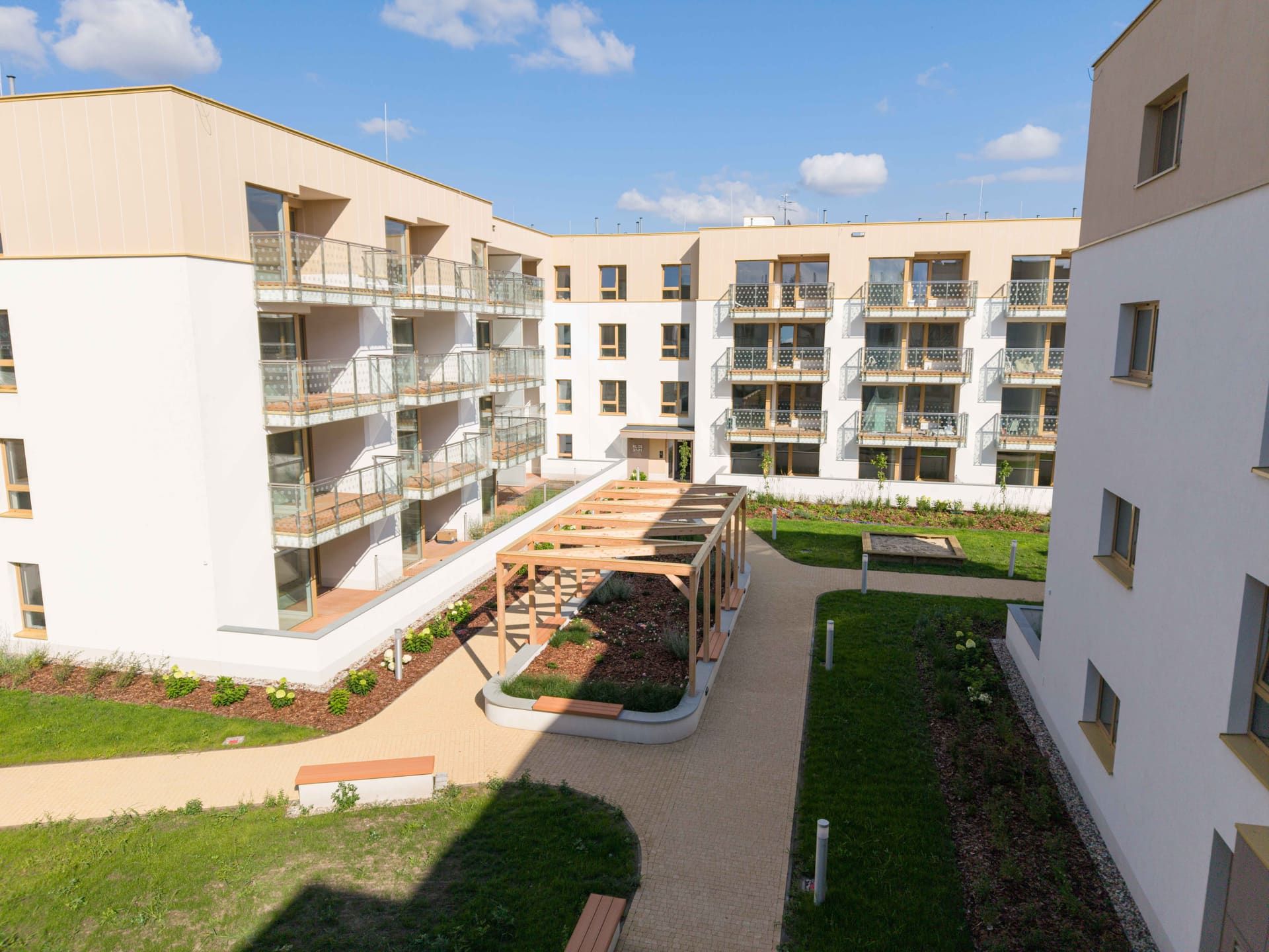 Zrealizowane zielone patio Nova Daliova z drewnianą pergolą, ławkami i trawnikami — Etap II